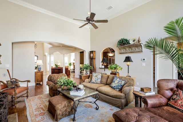 living room featuring visible vents, wood finished floors, arched walkways, crown molding, and a towering ceiling