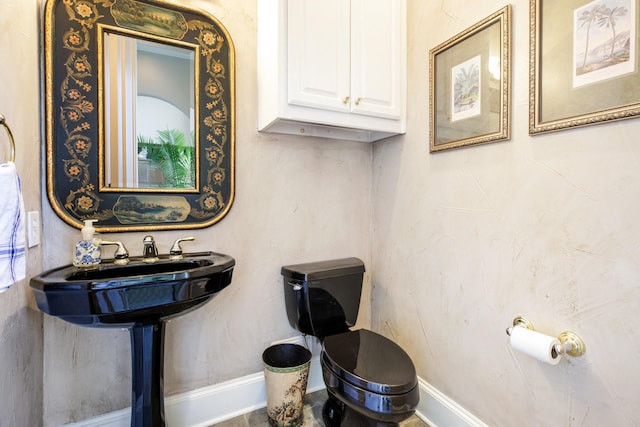 half bathroom featuring toilet, baseboards, and a sink