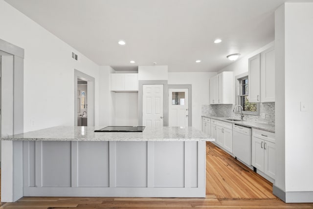 kitchen featuring dishwasher, a peninsula, light stone countertops, and a sink