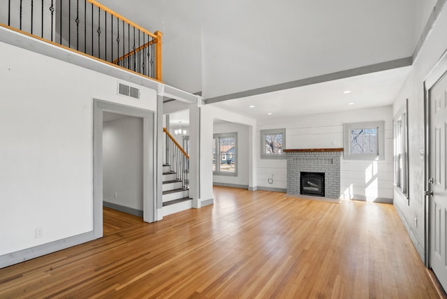 unfurnished living room with light wood finished floors, visible vents, a brick fireplace, baseboards, and stairs