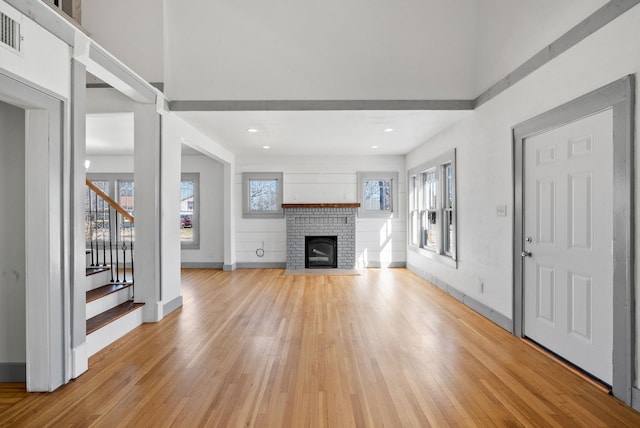 unfurnished living room featuring stairway, a fireplace, baseboards, and light wood-style floors