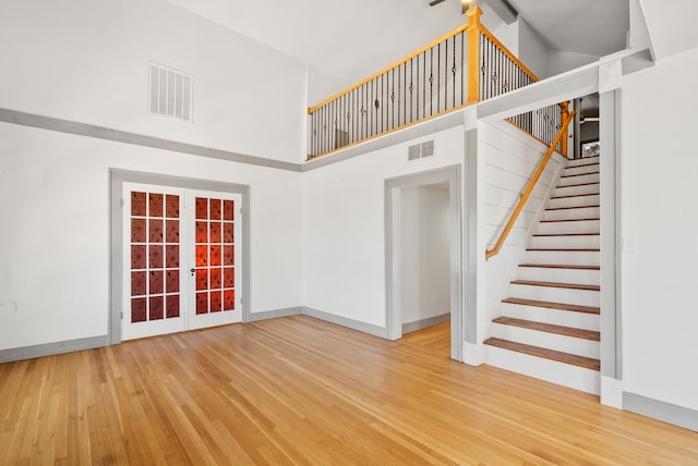 unfurnished living room featuring visible vents, a high ceiling, wood finished floors, and french doors