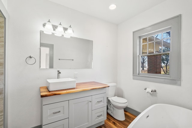 bathroom with vanity, wood finished floors, baseboards, a freestanding tub, and toilet