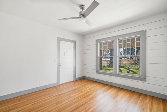 spare room with wooden walls, light wood-style flooring, a ceiling fan, and baseboards