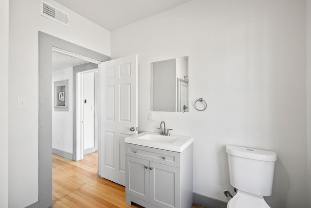 bathroom with vanity, wood finished floors, visible vents, baseboards, and toilet