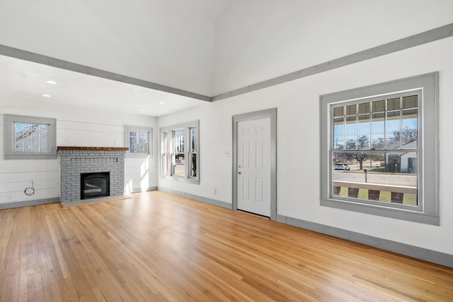 unfurnished living room with a towering ceiling, baseboards, hardwood / wood-style floors, and a fireplace