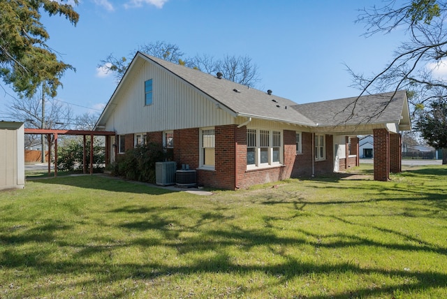 back of property with cooling unit, brick siding, a lawn, and a shingled roof