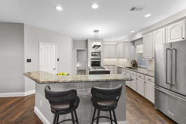 kitchen featuring light stone counters, dark wood-style floors, a center island, appliances with stainless steel finishes, and decorative backsplash