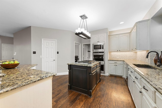 kitchen with light stone counters, a sink, dark wood-type flooring, appliances with stainless steel finishes, and backsplash