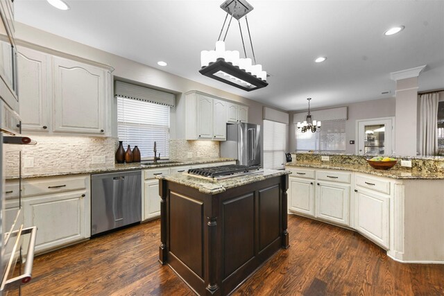 kitchen with a sink, a kitchen island, dark wood-style floors, appliances with stainless steel finishes, and a chandelier