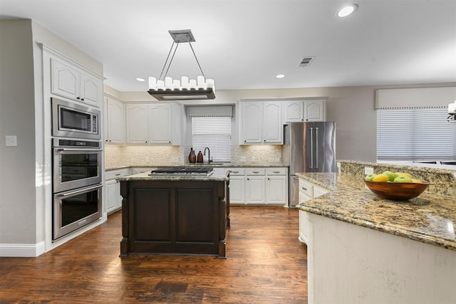 kitchen featuring visible vents, dark wood-type flooring, light stone counters, stainless steel appliances, and a sink