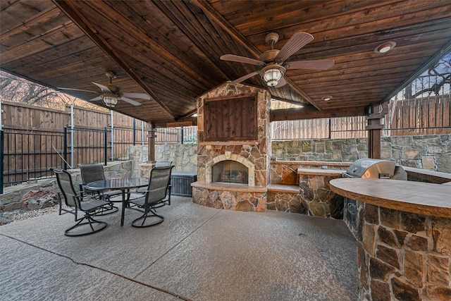 view of patio featuring area for grilling, a ceiling fan, fence, an outdoor stone fireplace, and outdoor dining area