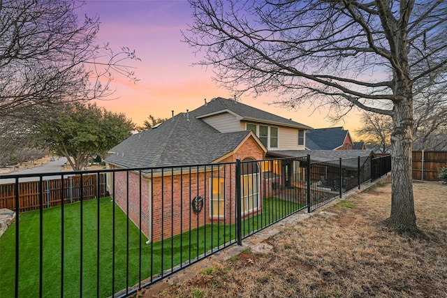 exterior space with a yard, brick siding, a fenced backyard, and a shingled roof