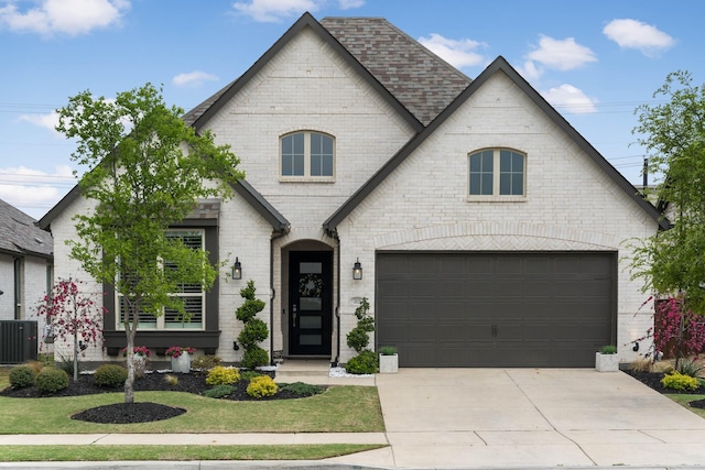 french provincial home with brick siding, concrete driveway, central air condition unit, and a front lawn