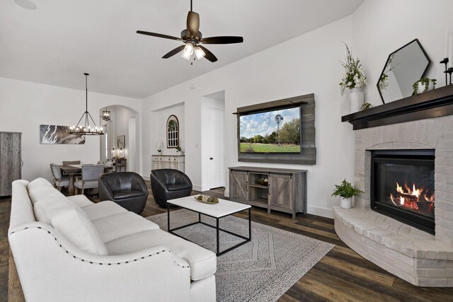 living room with ceiling fan with notable chandelier, baseboards, arched walkways, a fireplace, and wood finished floors