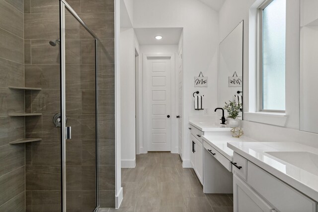 full bathroom with double vanity, a sink, a stall shower, and baseboards