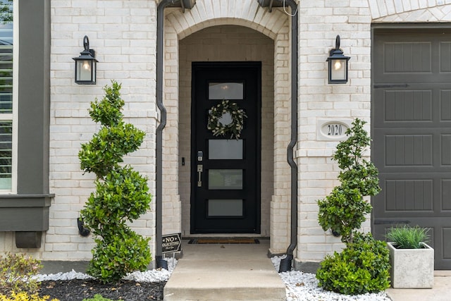 entrance to property featuring an attached garage and brick siding