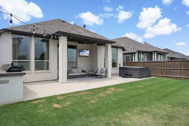 rear view of property featuring a ceiling fan, brick siding, a hot tub, a patio, and a yard