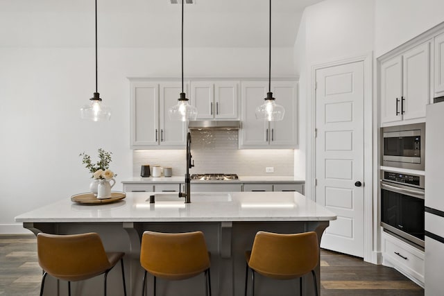 kitchen featuring tasteful backsplash, a kitchen breakfast bar, stainless steel appliances, decorative light fixtures, and dark wood-style flooring