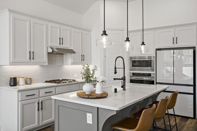 kitchen featuring decorative backsplash, white cabinets, stainless steel appliances, under cabinet range hood, and a breakfast bar area