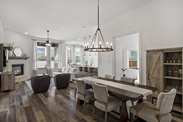 dining space featuring ceiling fan with notable chandelier, a brick fireplace, dark wood-style floors, and recessed lighting