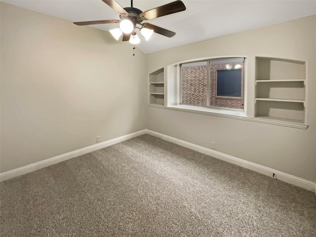 carpeted empty room with baseboards, built in shelves, a ceiling fan, and vaulted ceiling