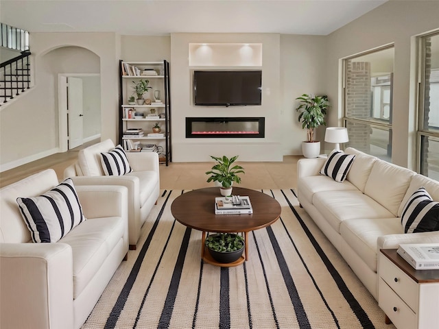 living room with arched walkways, a glass covered fireplace, and stairs