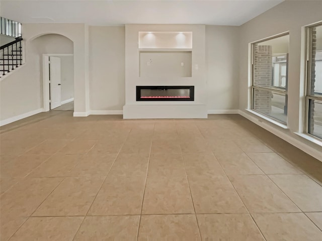 unfurnished living room featuring a glass covered fireplace, stairway, baseboards, and tile patterned flooring