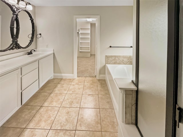 full bathroom featuring a walk in closet, baseboards, a bath, tile patterned floors, and vanity