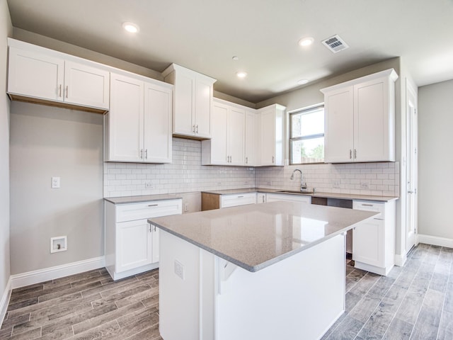 kitchen with light stone counters, visible vents, wood finish floors, a sink, and white cabinets