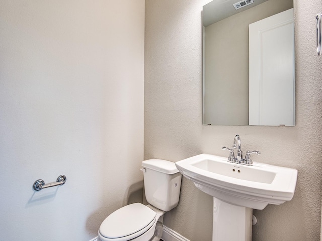 half bath featuring toilet, a textured wall, and visible vents