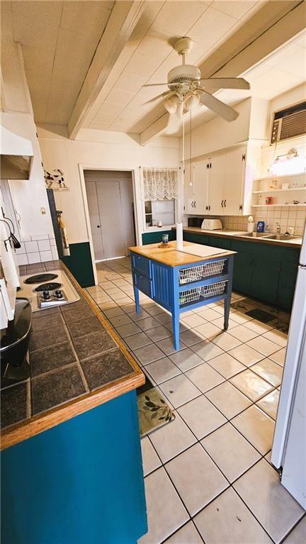 kitchen with backsplash, tile countertops, light tile patterned floors, beam ceiling, and white cabinets