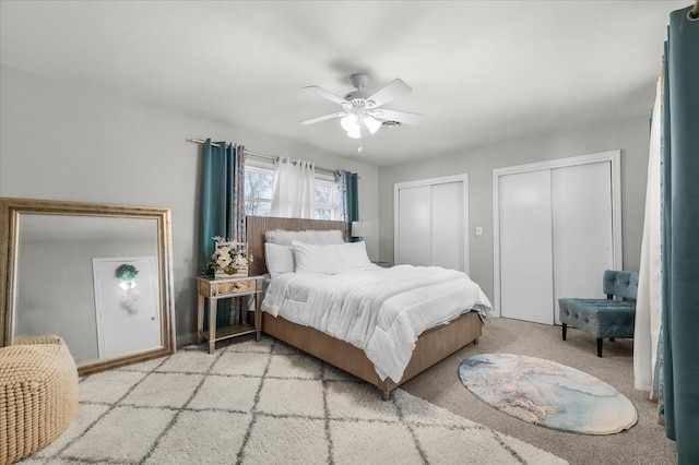 bedroom featuring light carpet, two closets, and a ceiling fan