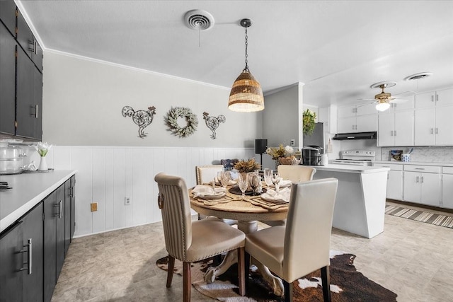 dining area with visible vents, a ceiling fan, ornamental molding, and wainscoting