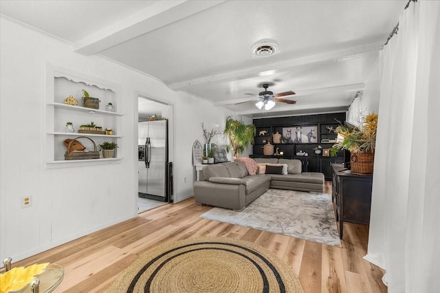 living area featuring built in shelves, a ceiling fan, wood finished floors, visible vents, and beamed ceiling