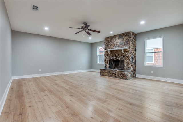 unfurnished living room with visible vents, light wood-style flooring, a stone fireplace, and ceiling fan