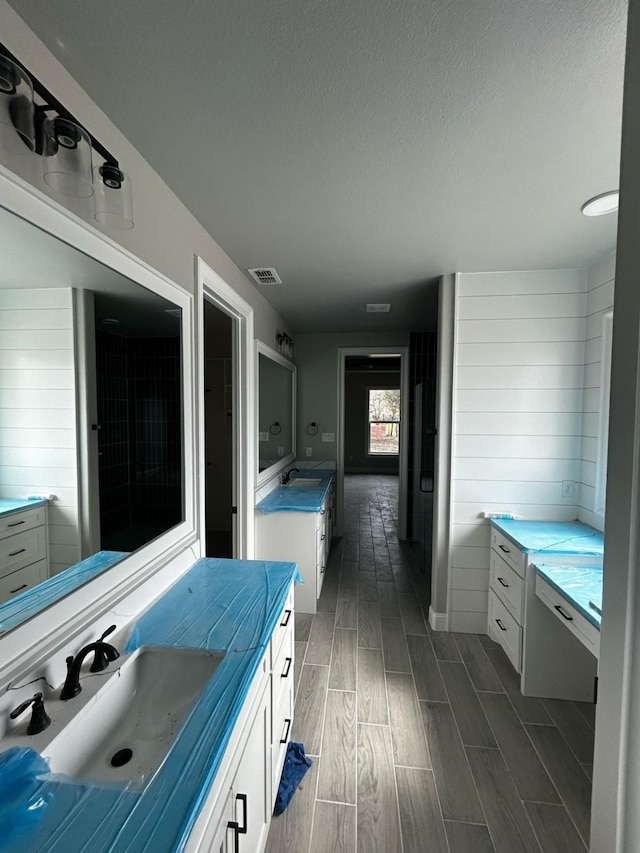 bathroom with a textured ceiling, vanity, visible vents, and wood tiled floor