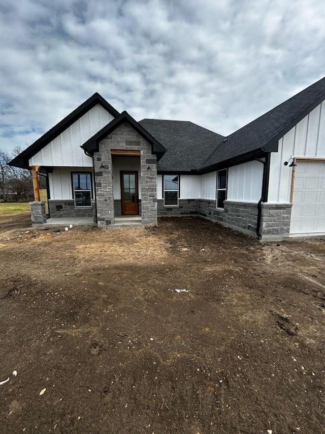 modern farmhouse style home featuring stone siding, board and batten siding, a shingled roof, and a garage