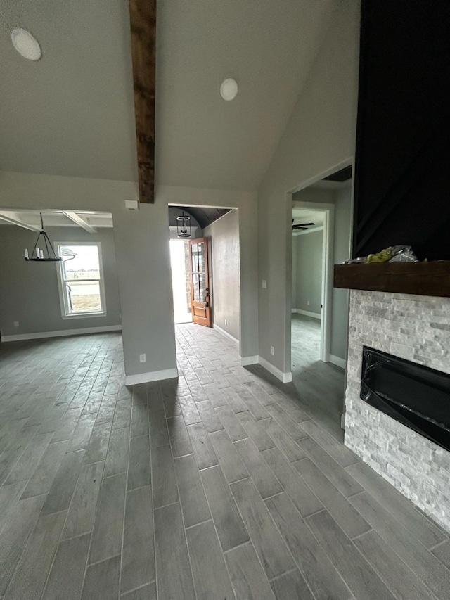 unfurnished living room featuring a stone fireplace, lofted ceiling with beams, and wood finish floors