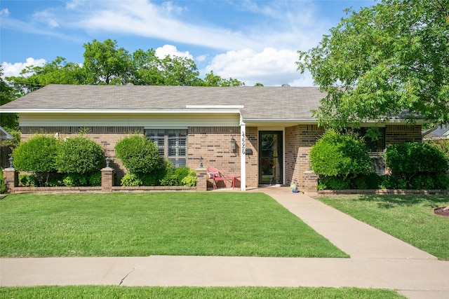 ranch-style home featuring brick siding, a front lawn, and roof with shingles