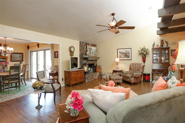 living room with wood finished floors, lofted ceiling, a stone fireplace, a textured ceiling, and ceiling fan with notable chandelier