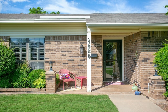 entrance to property with brick siding and a shingled roof