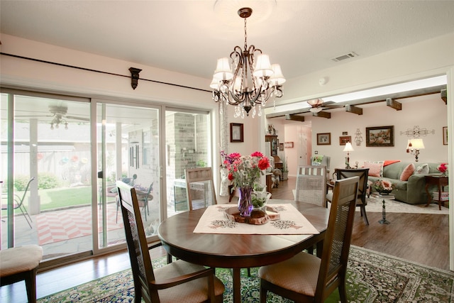 dining space featuring ceiling fan with notable chandelier, beamed ceiling, wood finished floors, and visible vents