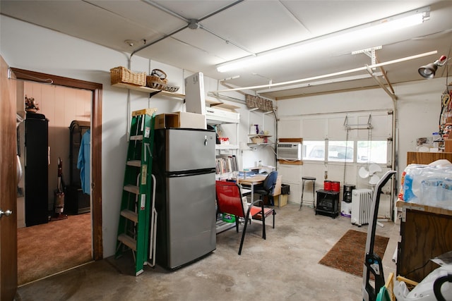 below grade area with radiator heating unit, freestanding refrigerator, and a wall mounted AC