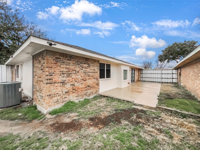 rear view of property with cooling unit, a patio, brick siding, and fence