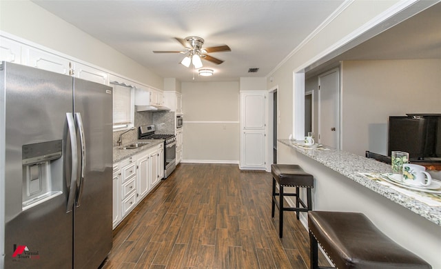 kitchen with a kitchen bar, dark wood-type flooring, a sink, stainless steel appliances, and white cabinets