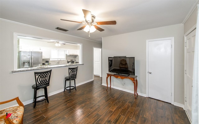 kitchen with dark wood-type flooring, appliances with stainless steel finishes, under cabinet range hood, a kitchen bar, and backsplash