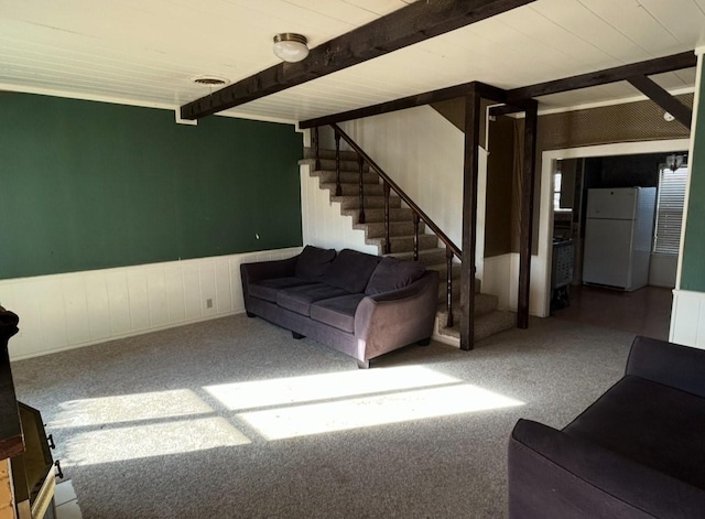 unfurnished living room featuring beamed ceiling, wainscoting, carpet flooring, and stairs