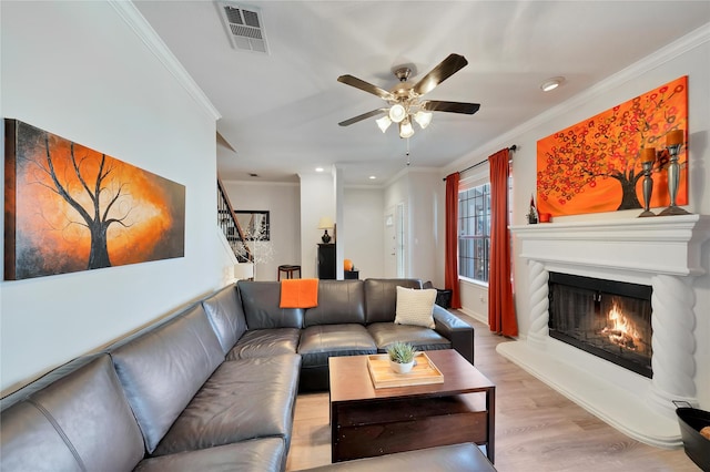 living room with visible vents, stairs, ornamental molding, a warm lit fireplace, and wood finished floors