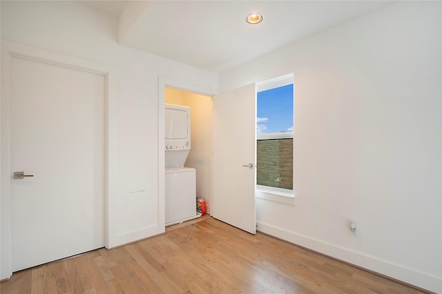 spare room featuring baseboards, stacked washer and clothes dryer, and light wood-style flooring